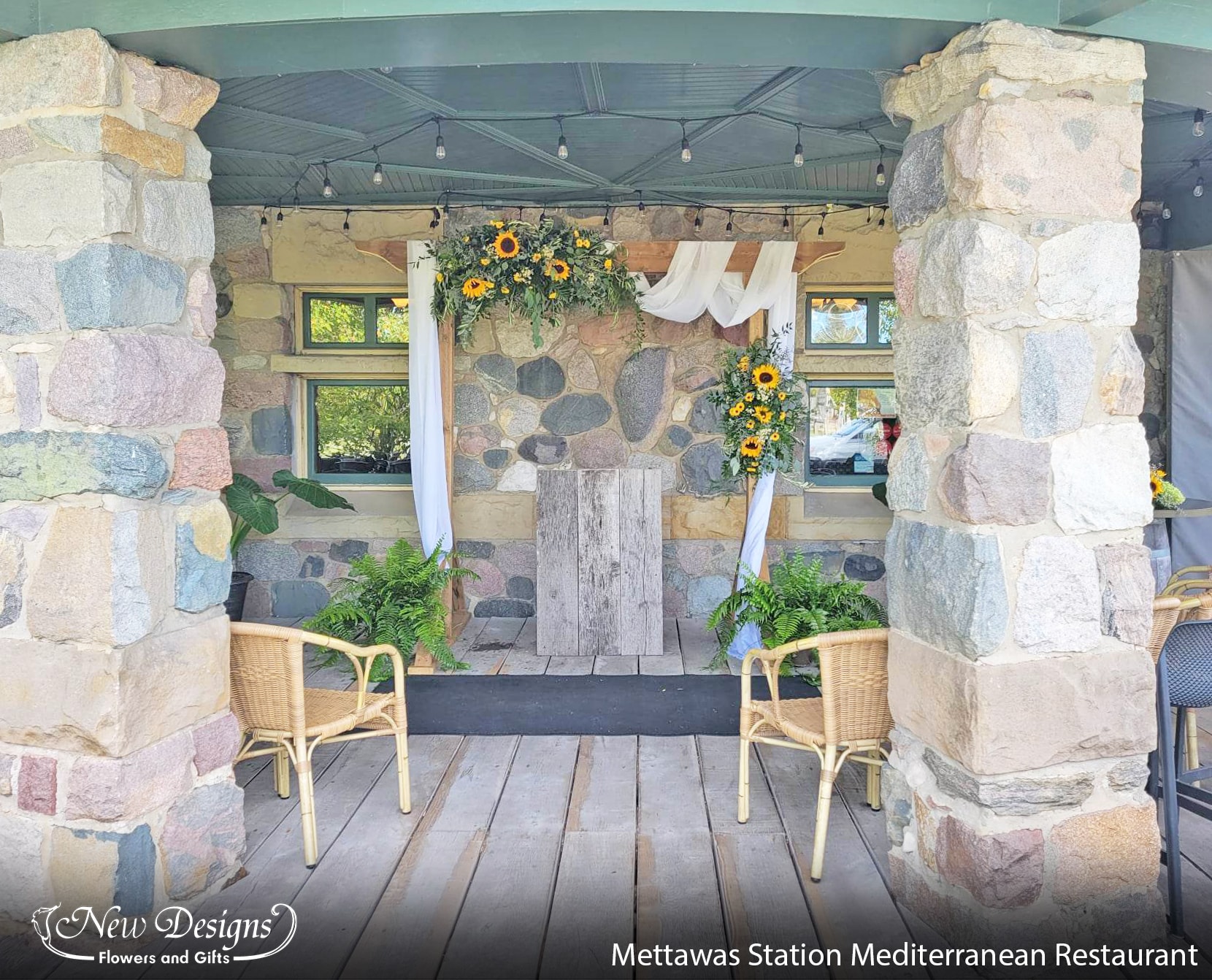 A square arch draped with white material, greenery and sunflowers sits under the rustic patio of Mettawas Train Station and Mediterranean Restaraunt in Kingsville.